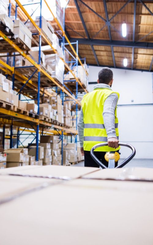 male-warehouse-worker-pulling-a-pallet-truck-PE8NHXJ-scaled